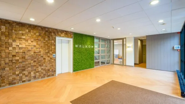 Ingang van een kantoor met een houten wand en een groene mosmuur met het woord "WELKOM".