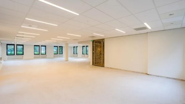 Een ruime, lege kantoorruimte met witte muren en grote ramen aan de Amalialaan.