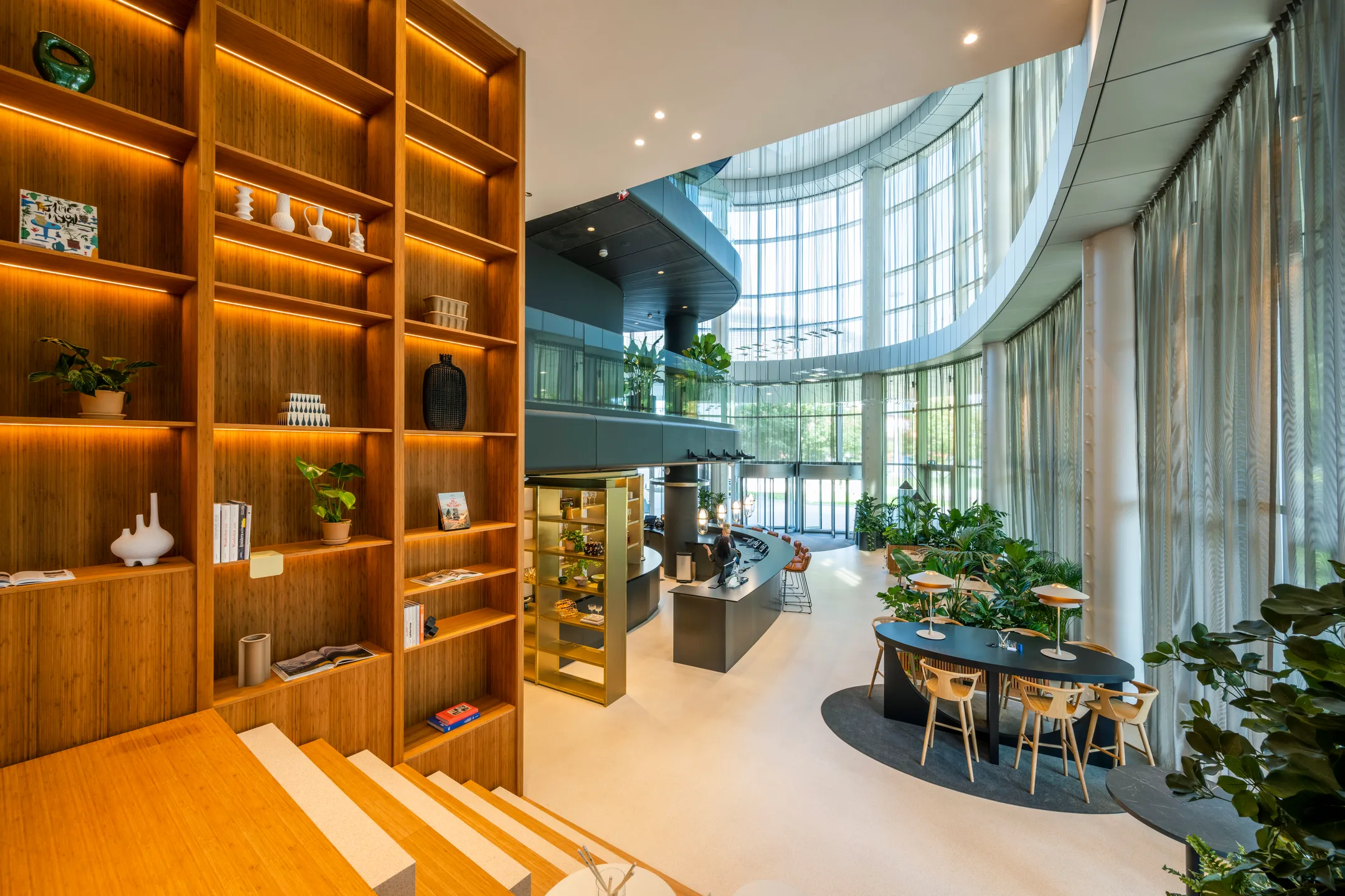 Een moderne, lichte kantoorruimte met houten wandrekken, planten, en een ronde glazen gevel.