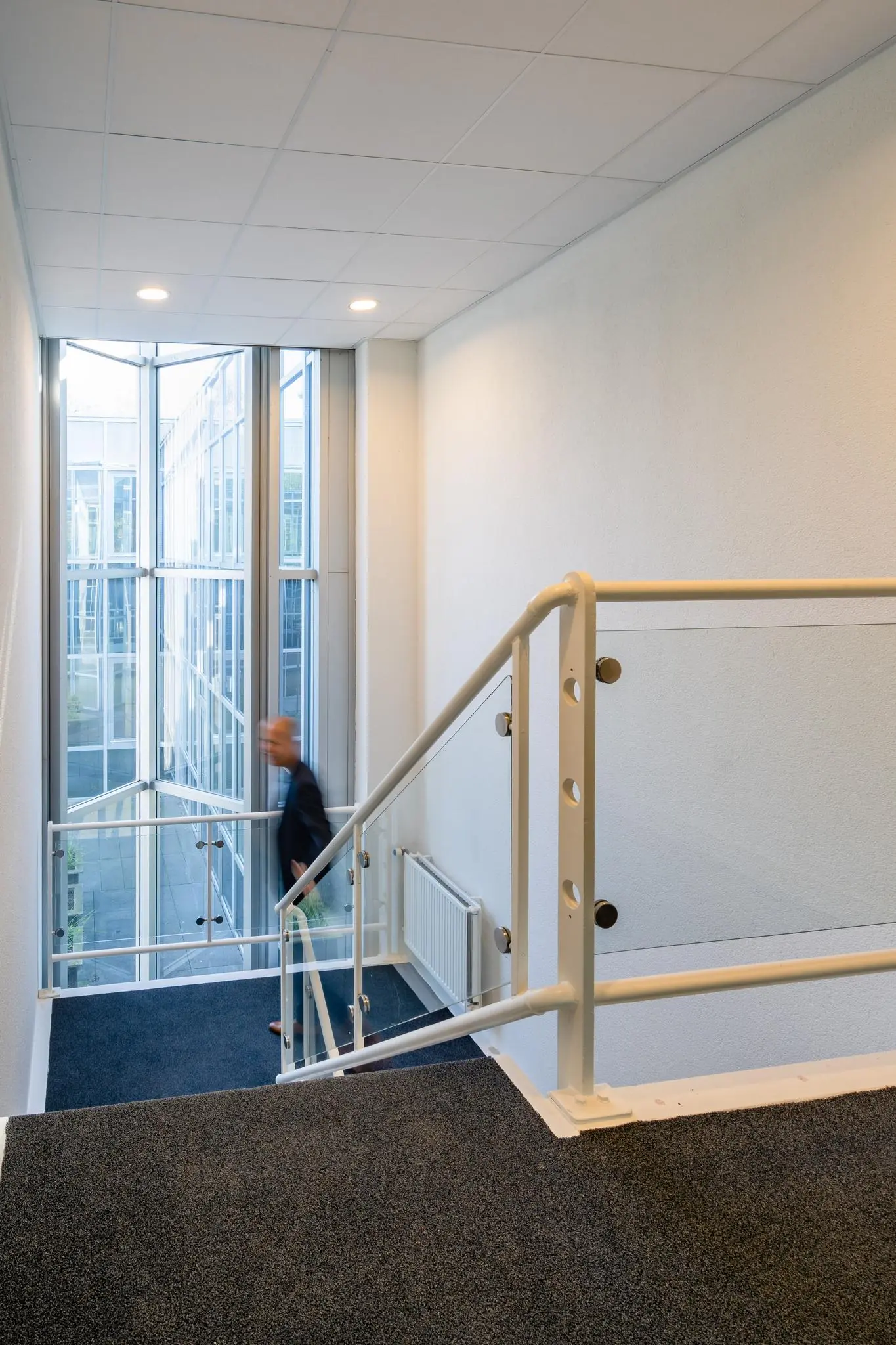 Een man loopt een trappenhuis op in een modern kantoorpand aan de Utrechtseweg met grote glazen ramen.