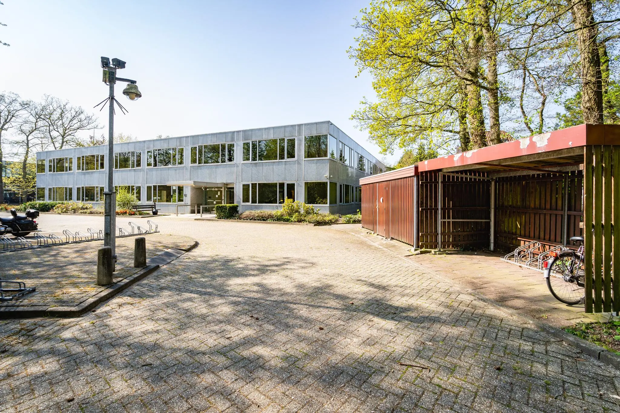 Voorzijde van een modern kantoorgebouw aan de Utrechtseweg met fietsenstalling en parkeerplaats.