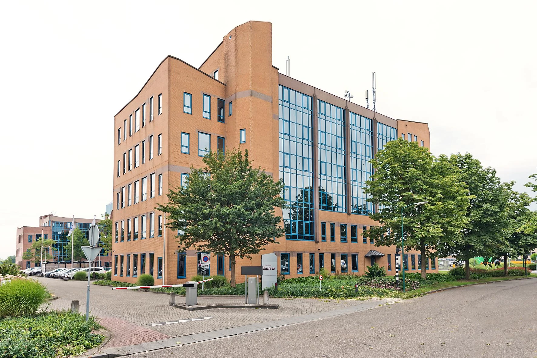 Modern kantoorgebouw aan het Kosterijland met grote ramen en omringd door groen.