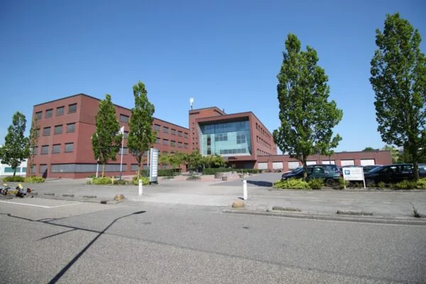 Modern kantoorgebouw aan de Pompmolenlaan met bakstenen gevel, grote ramen en omliggende parkeerplaatsen en bomen.