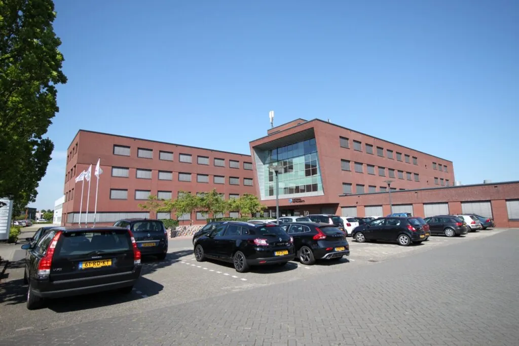 Een modern kantoorgebouw aan de Pompmolenlaan met een parkeerterrein op de voorgrond.