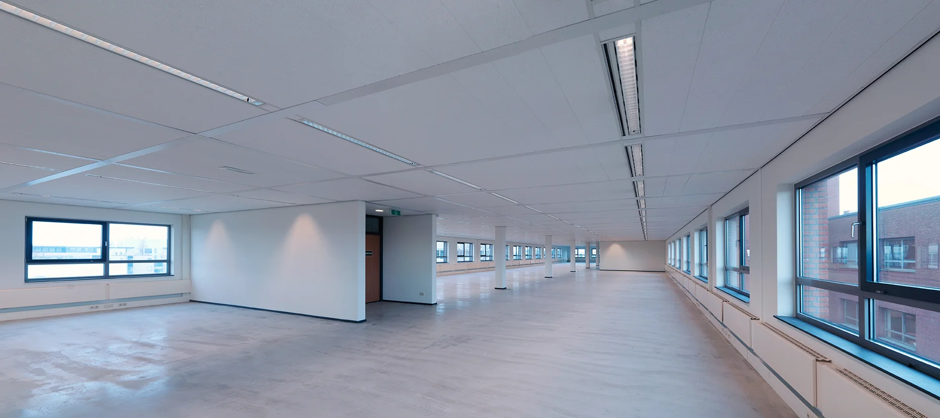 Lichte, lege kantoorruimte op de Pompmolenlaan met grote ramen en systeemplafond.