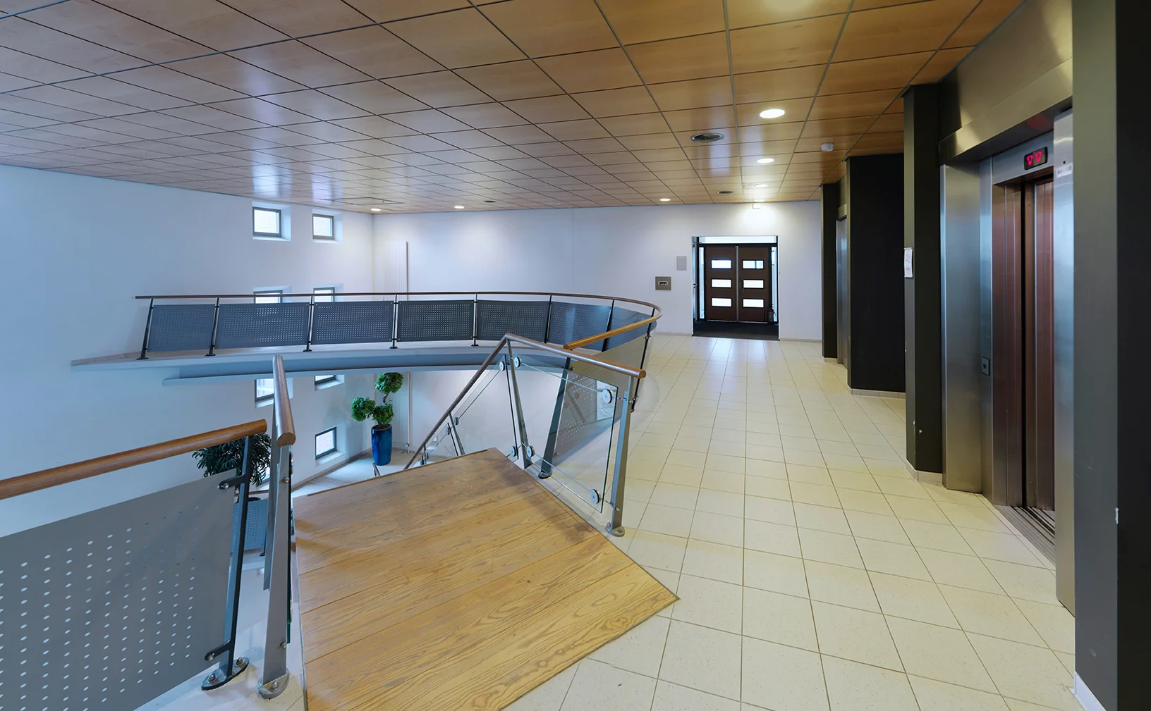 Moderne, lichte hal met houten trap, lift en glazen balustrade aan de Pompmolenlaan.