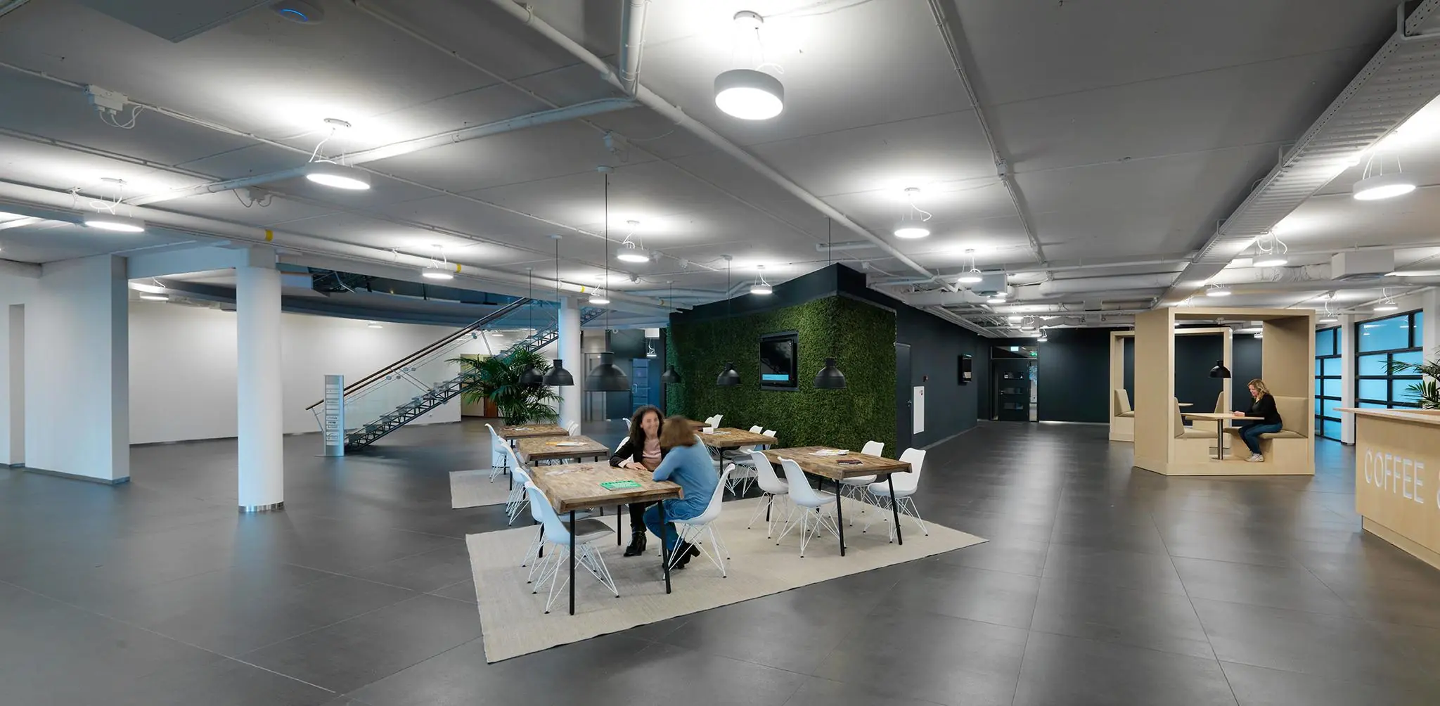 Moderne en ruimtelijke kantoorlounge aan de Pompmolenlaan met zitruimtes, een koffiebar en groene wand.