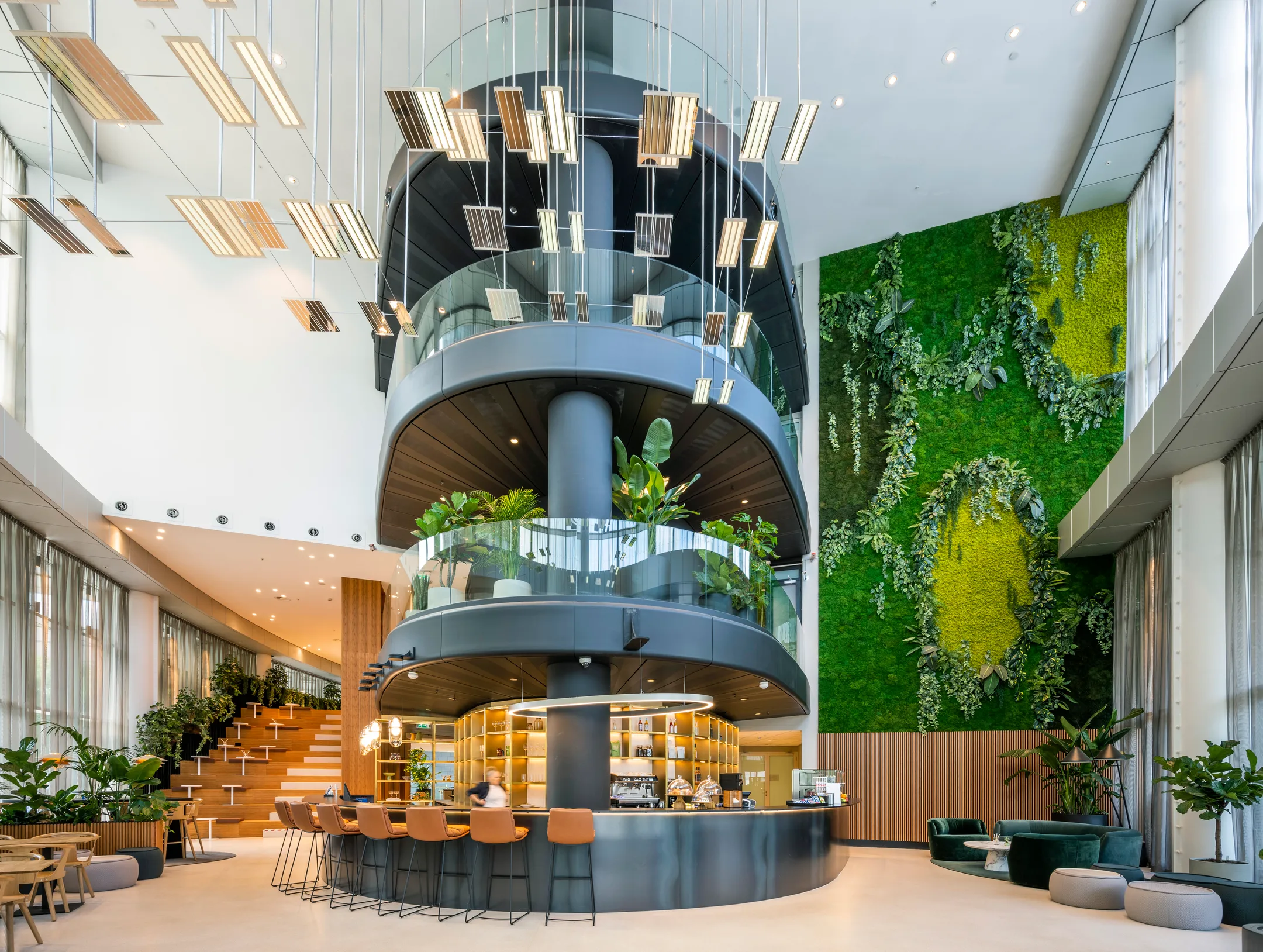 Een moderne, open ruimte met een ronde, meerlaagse structuur, groene plantenwand, en een stijlvol ingerichte bar en zitgedeelte.
