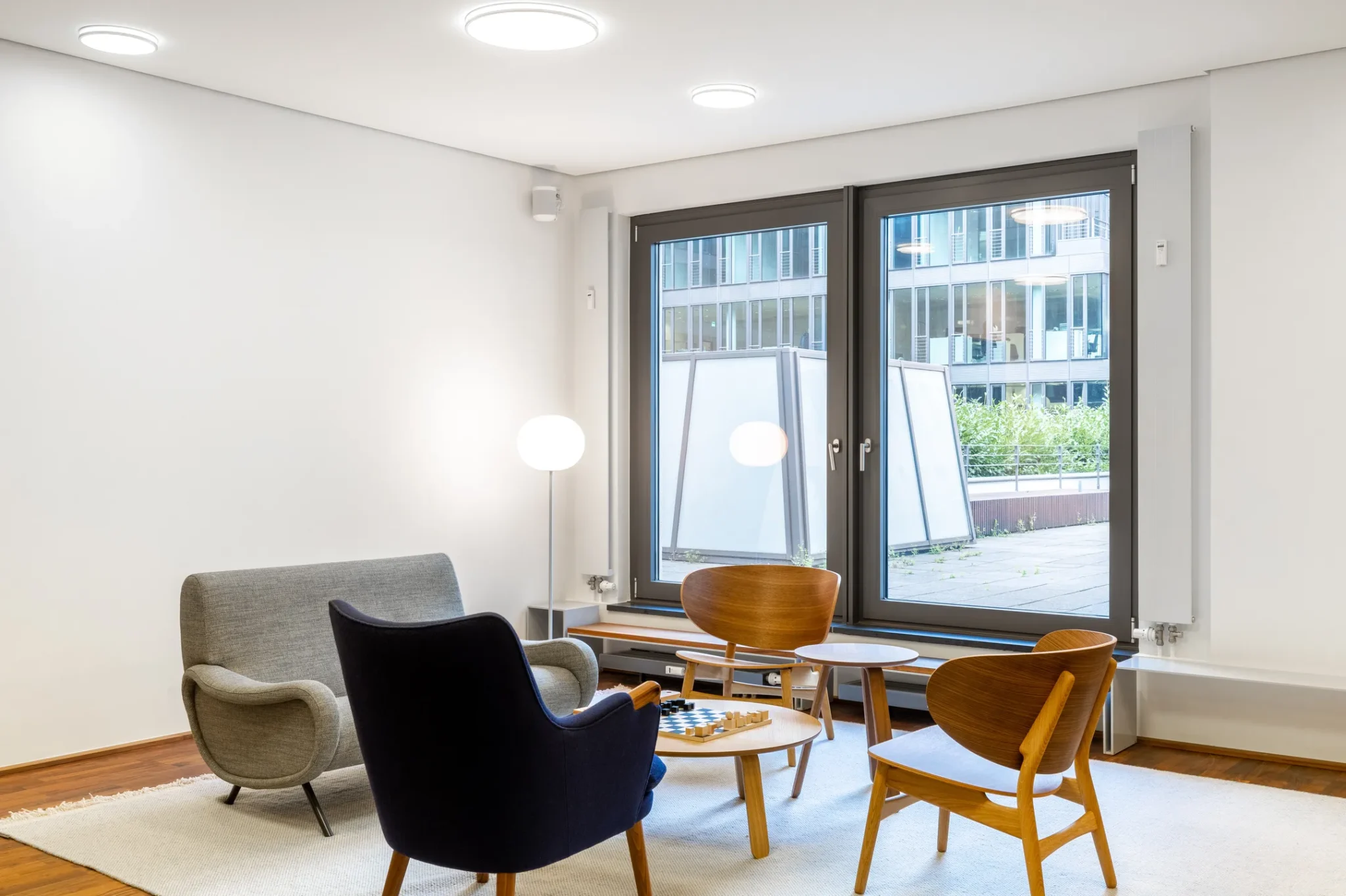 Moderne wachtruimte met designmeubilair, grote ramen en uitzicht op een binnenplaats.