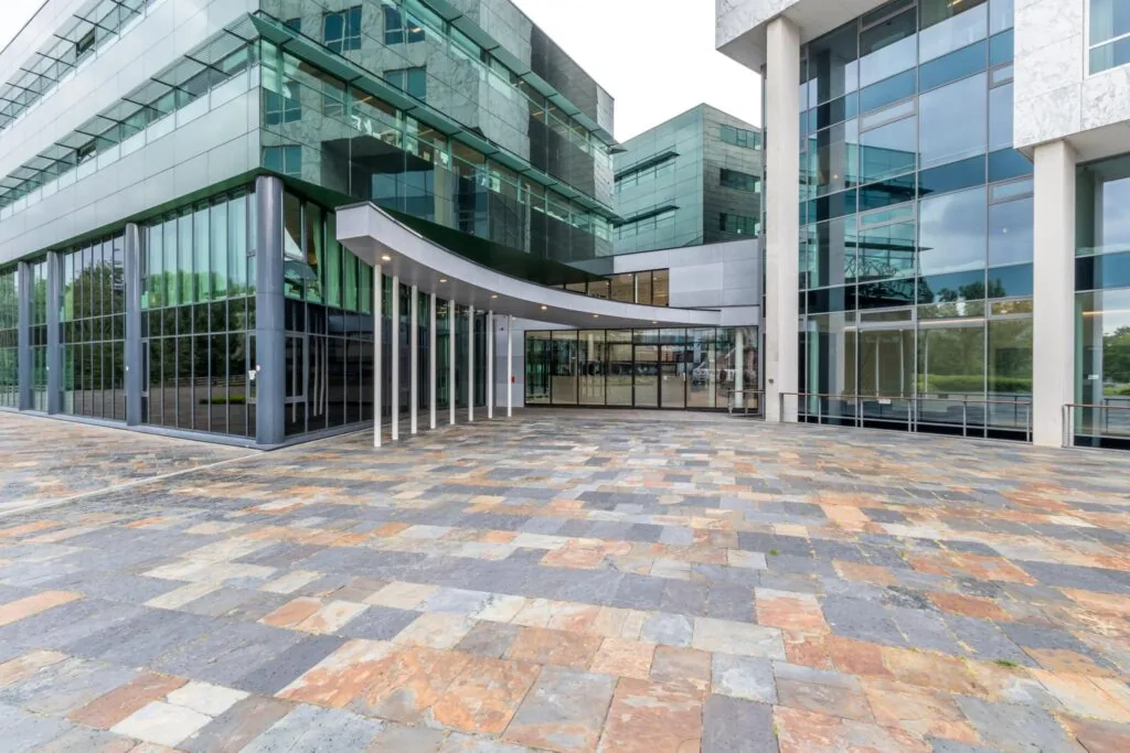 Moderne glazen entree van een kantoorgebouw op het Herculesplein met kleurrijk betegeld voorplein.