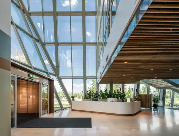 Moderne entreehal met glazen gevel, houten plafond en een receptiebalie met planten.