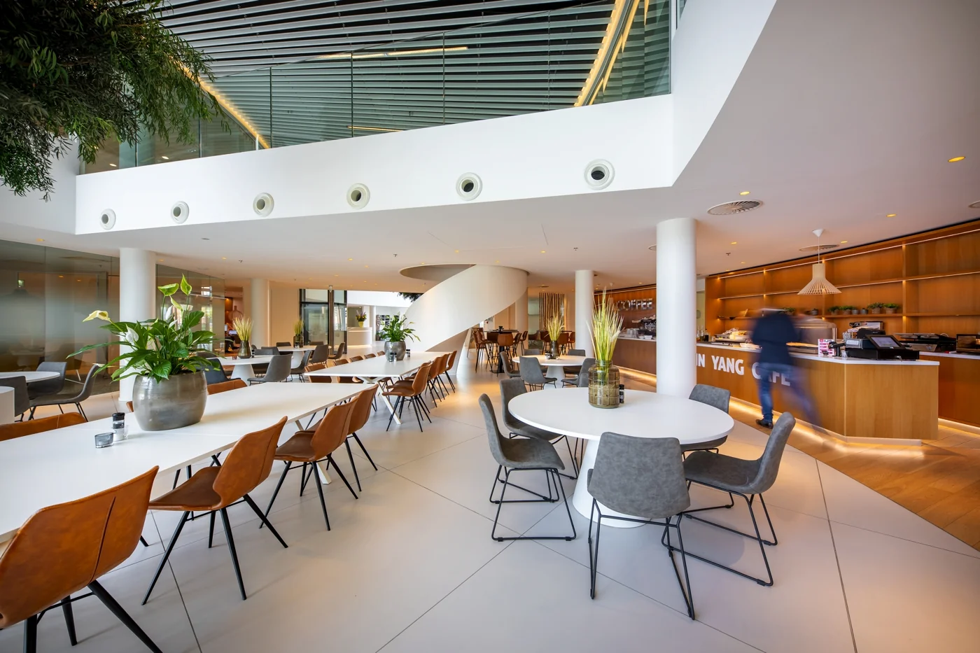 Een moderne, lichte kantoorlounge met tafels, stoelen en een caféhoek.