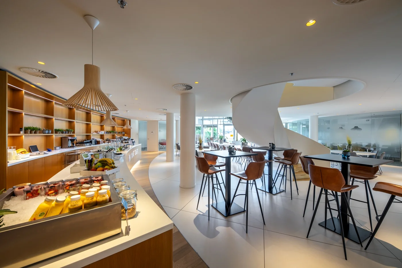 Een moderne, ruime kantine met hoge tafels en een opvallende wenteltrap.