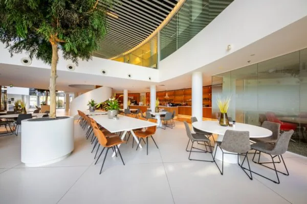 Een moderne, open kantoorlobby met een zitgelegenheid, planten en een brede wenteltrap.