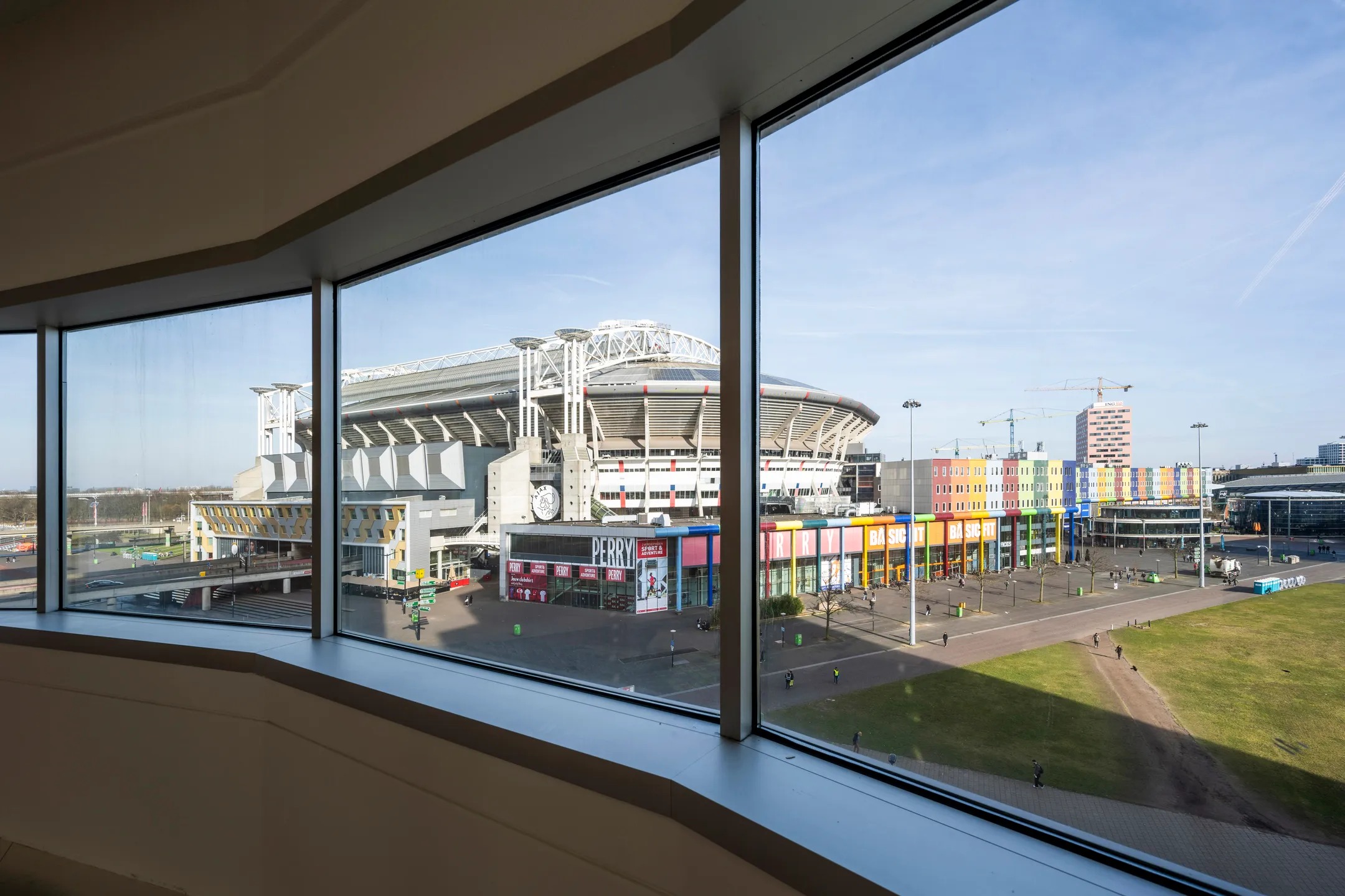 Uitzicht vanuit een gebouw op de Johan Cruijff ArenA en een kleurrijk winkelcentrum in Amsterdam.