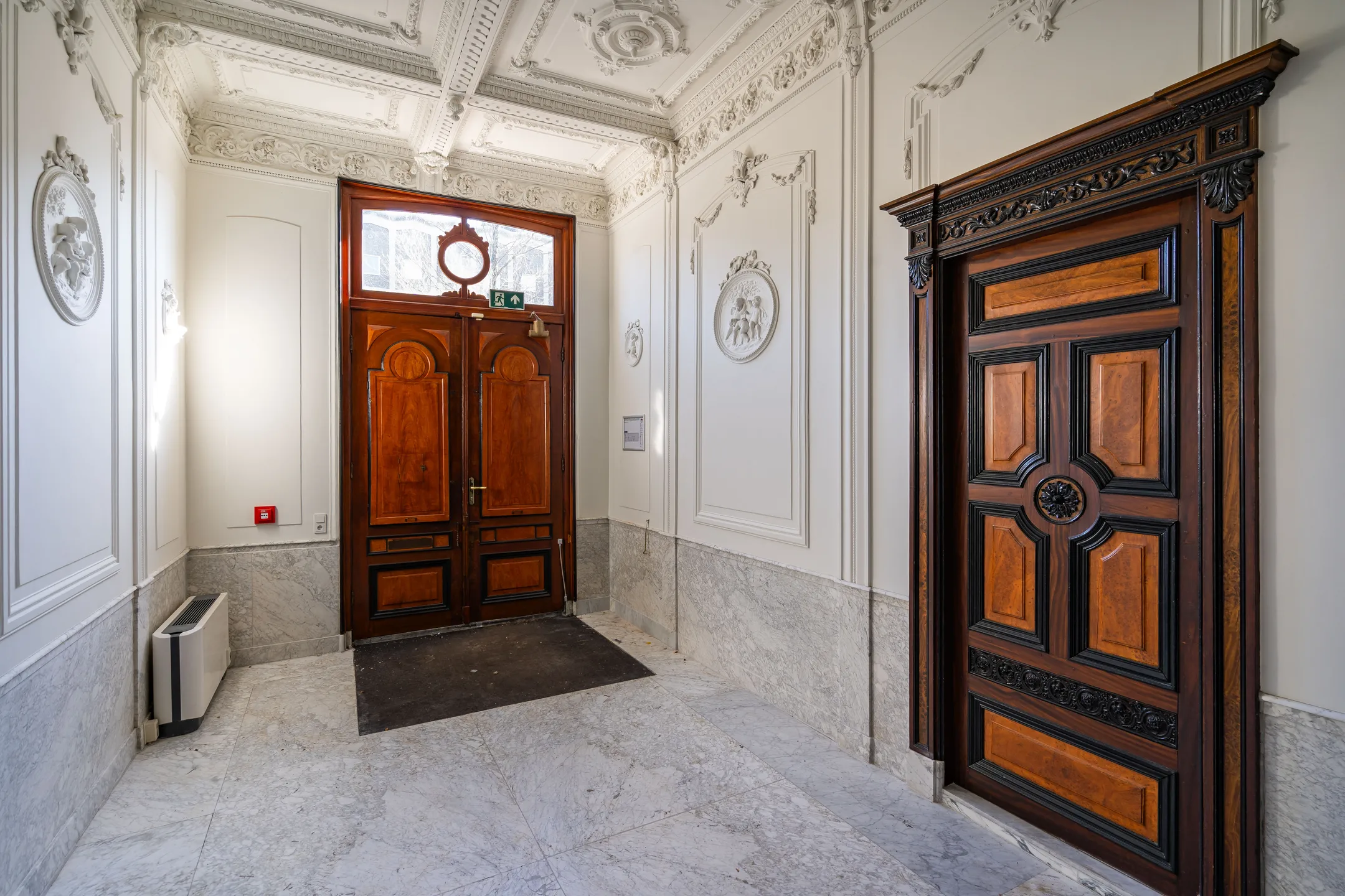 Een elegante hal met gedetailleerd plafond en houten deuren.