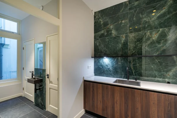 Moderne keuken met groene marmeren achterwand en houten kastdeuren.