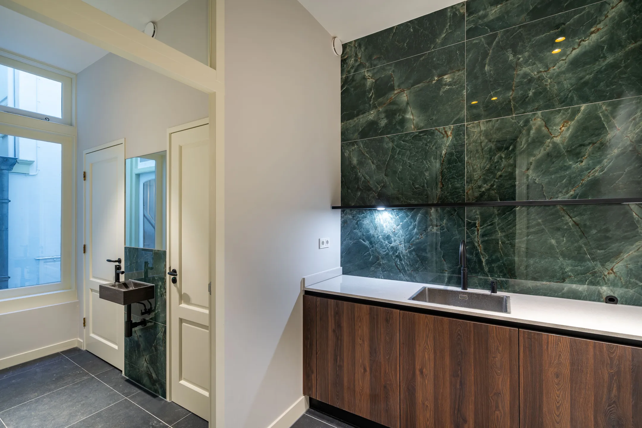 Moderne keuken met groene marmeren achterwand en houten kastdeuren.