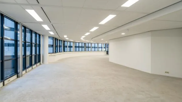 Leeg kantoorinterieur met grote ramen en witte muren.