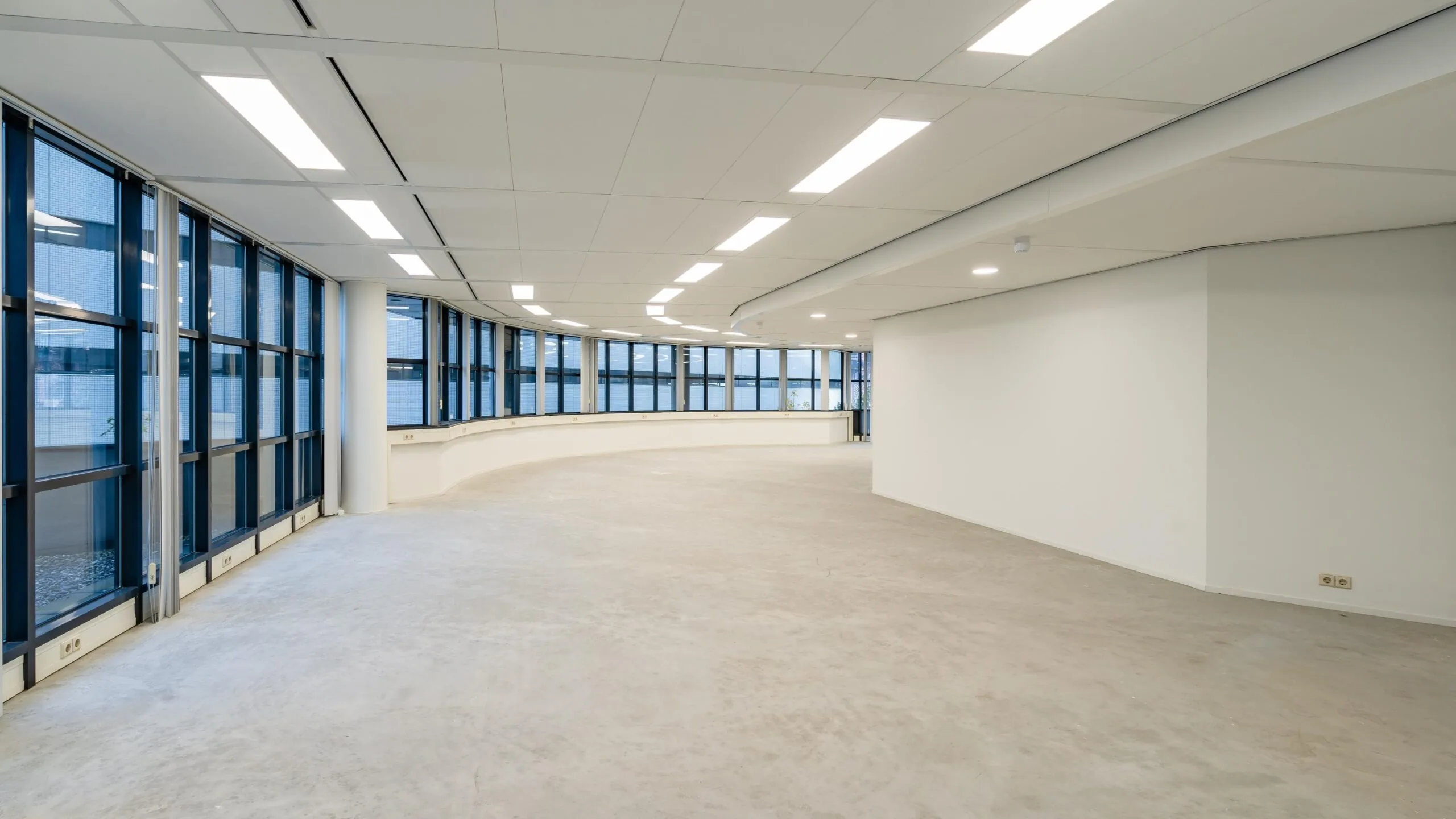 Leeg kantoorinterieur met grote ramen en witte muren.
