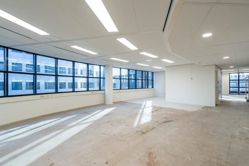 Lege kantoorruimte met grote ramen en witte muren in het Weena-gebouw.