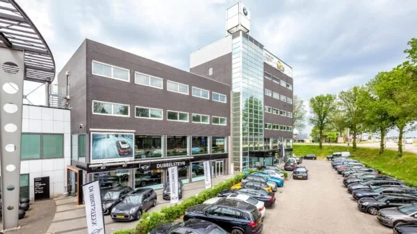 Voorgevel van het Dubbelsteyn autobedrijf aan de Mijlweg met geparkeerde auto’s op het terrein.