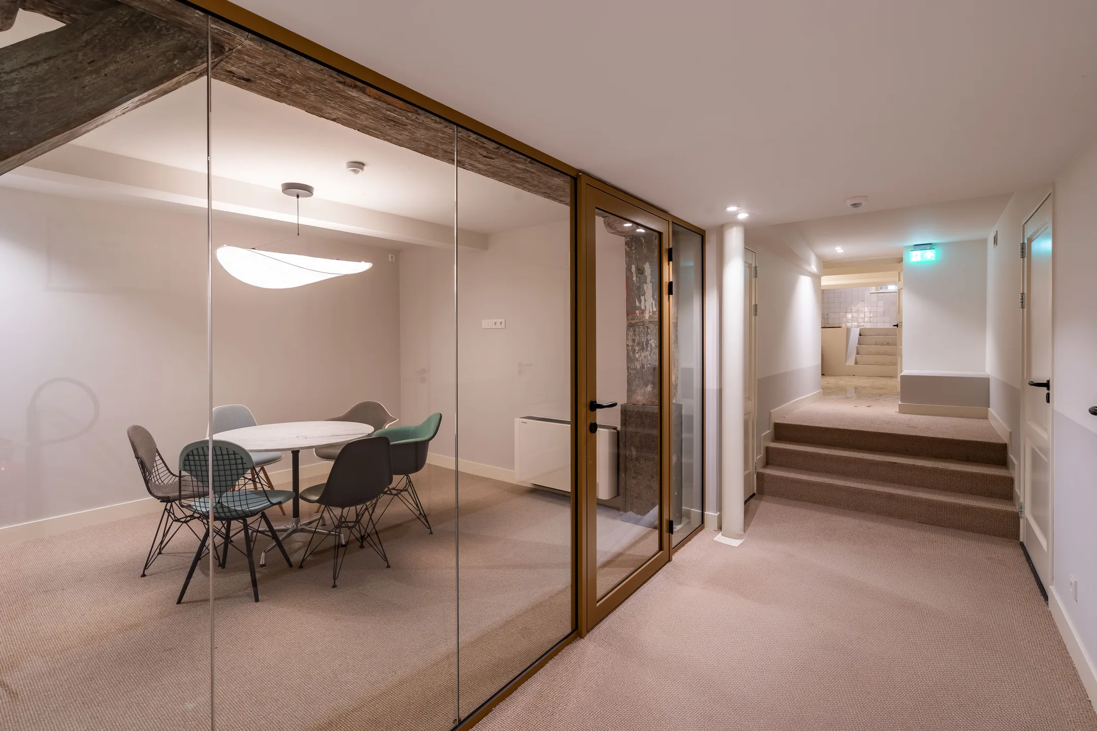 Een moderne vergaderruimte met glazen wand en ronde tafel met stoelen in een verlichte gang.