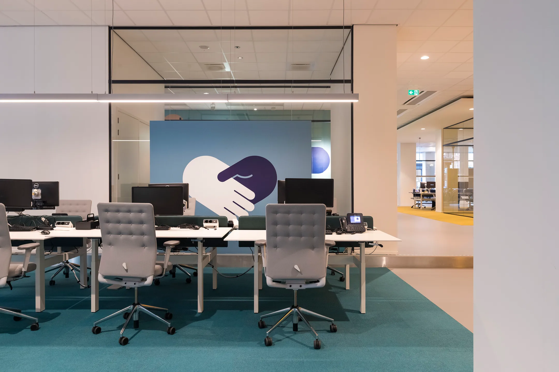 Een moderne kantoorruimte met bureaus, stoelen en een grote muurafbeelding van een handdruk.