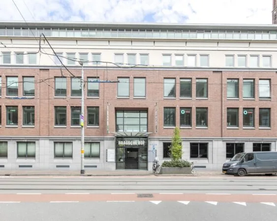 Voorgevel van het kantoorgebouw 'Haagse Hof' aan een trambaan met geparkeerde fietsen en busje.