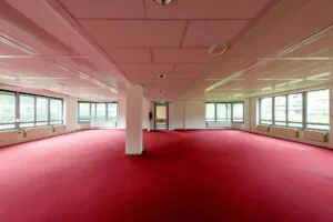 Lege kantoorruimte aan de Meesterlottelaan met rode vloerbedekking en grote ramen rondom.
