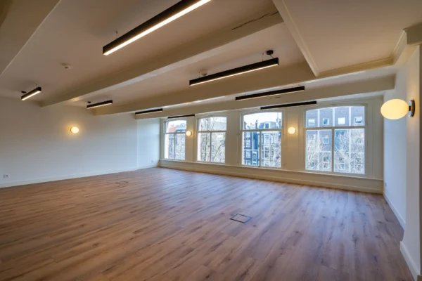 Lege kantoorruimte met houten vloer en grote ramen die uitkijken op gebouwen buiten.