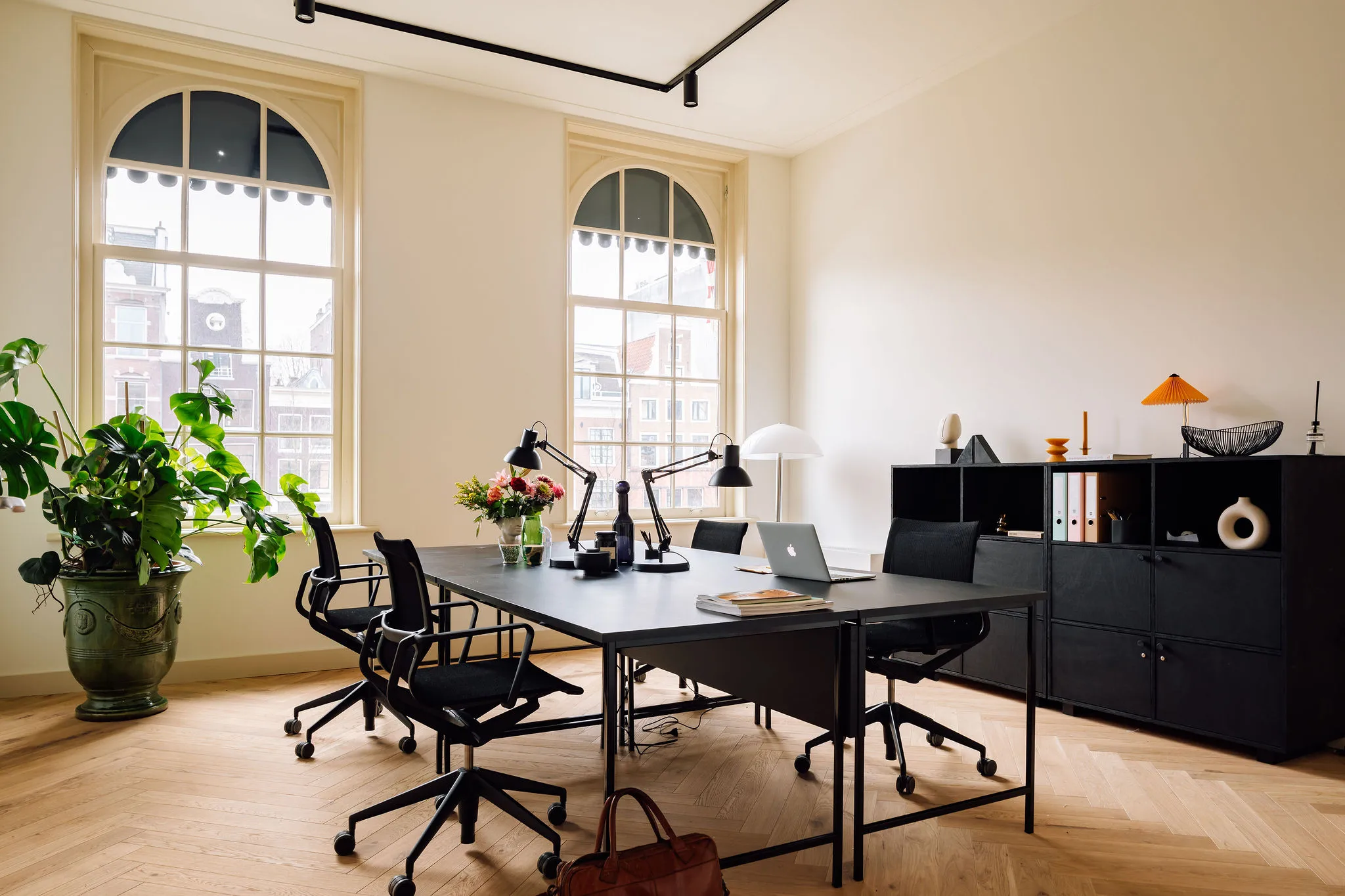 Een modern kantoor met een grote tafel, meerdere stoelen, decoratieve objecten, planten en grote ramen die uitzicht bieden op een stadsgezicht.