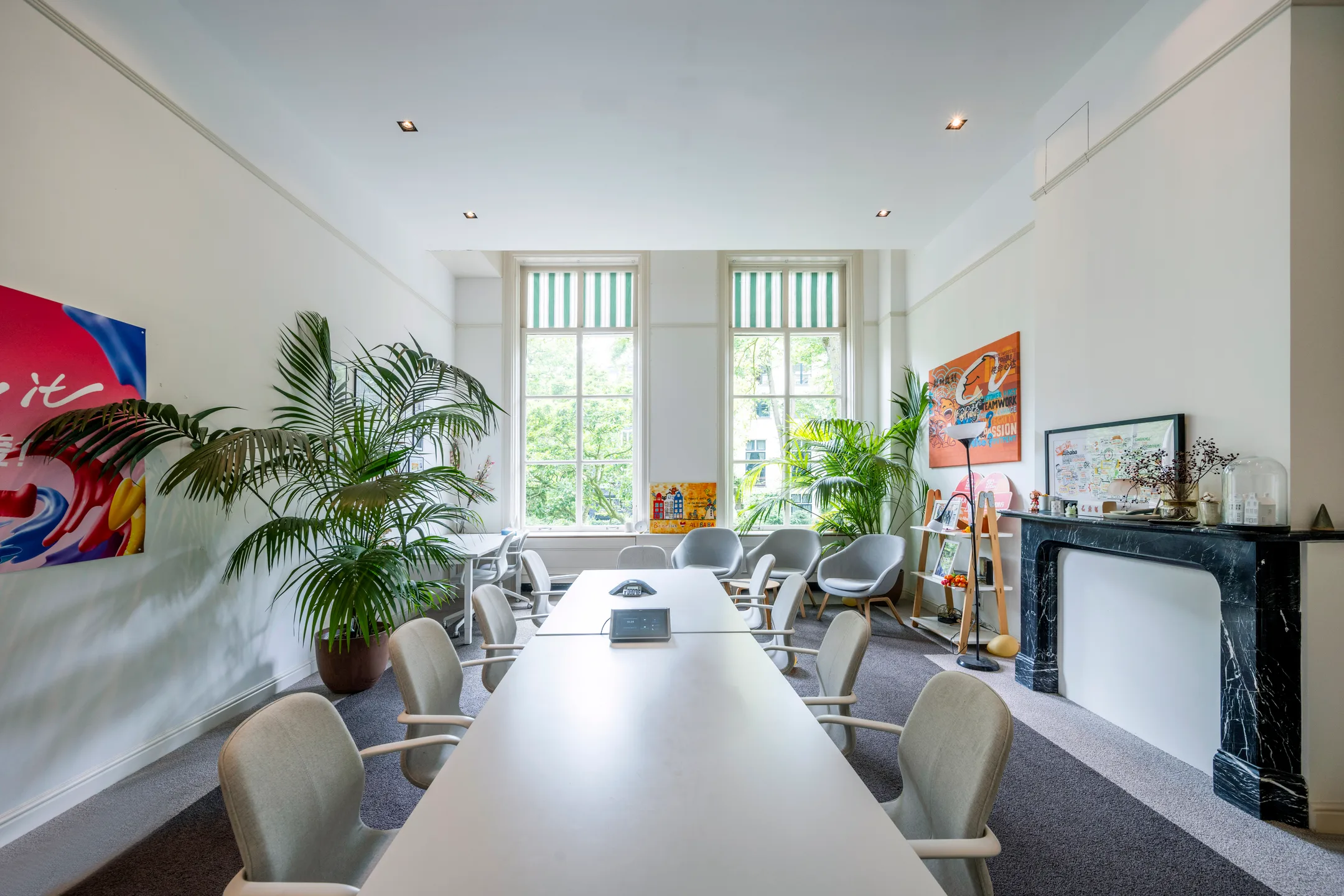 Vergaderruimte met een lange tafel, moderne stoelen, grote ramen en groene planten.