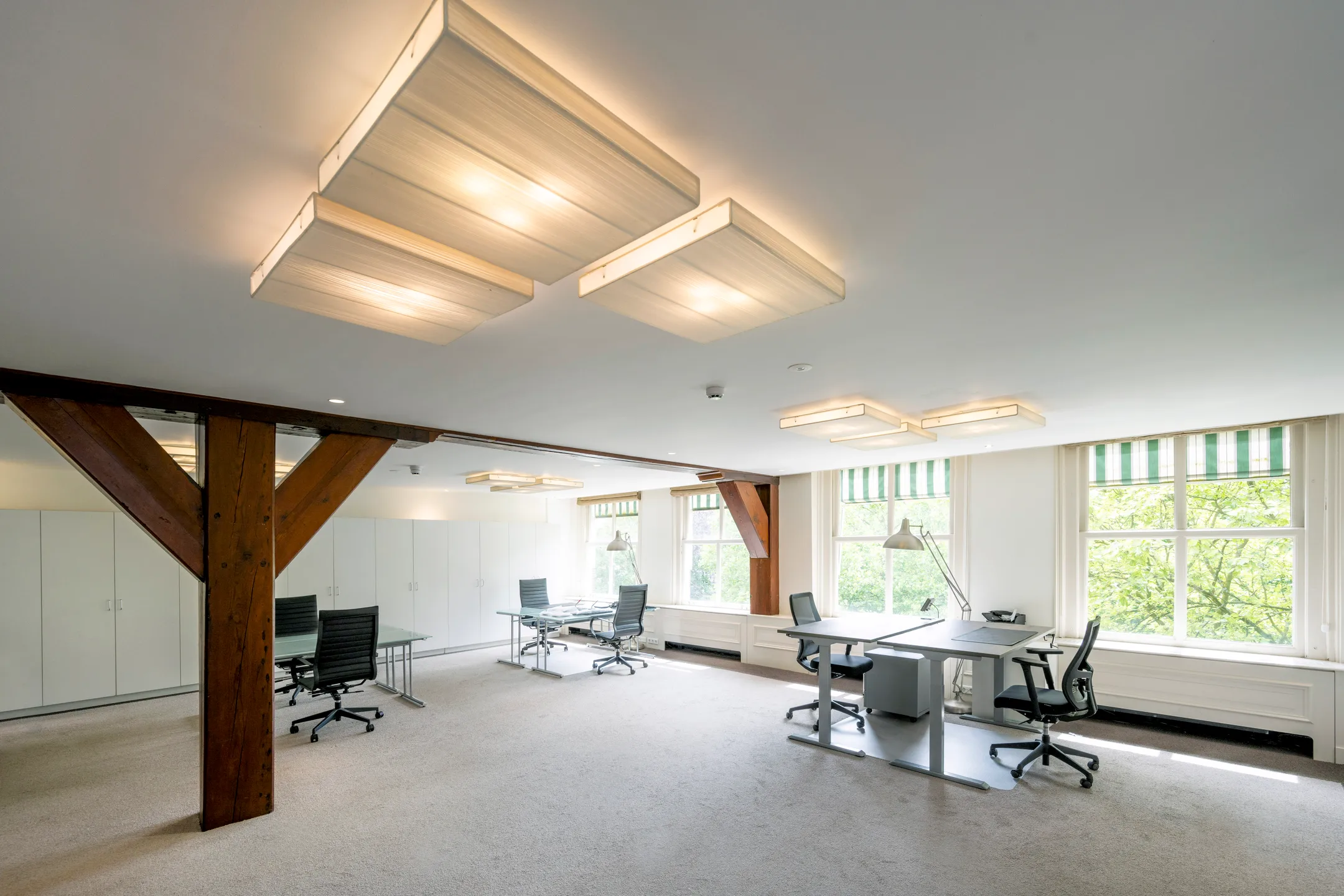 Een ruim en licht kantoor met moderne bureaus, stoelen en grote ramen met uitzicht op groen.