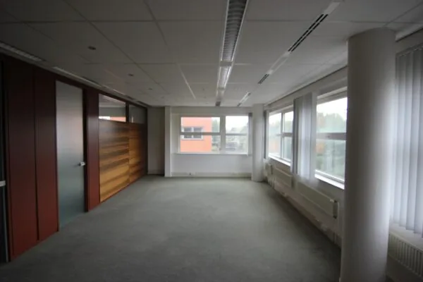 Leeg kantoor met grote ramen, systeemplafond en glazen deur met houten wandpanelen.