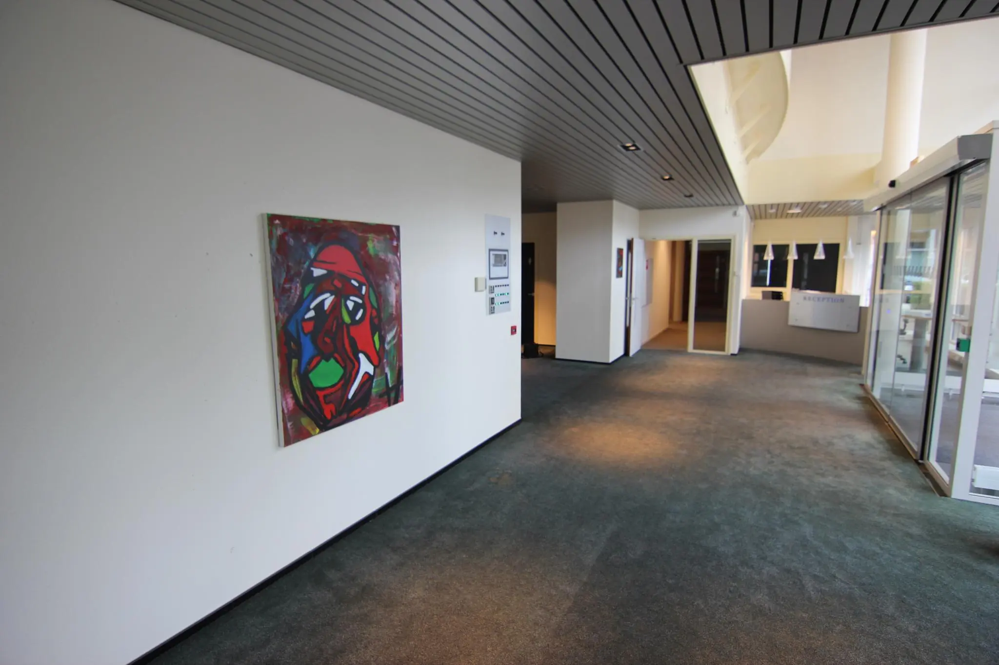 Hal met tapijtvloer en moderne kunst aan de muur, met zicht op een receptiebalie in de achtergrond.