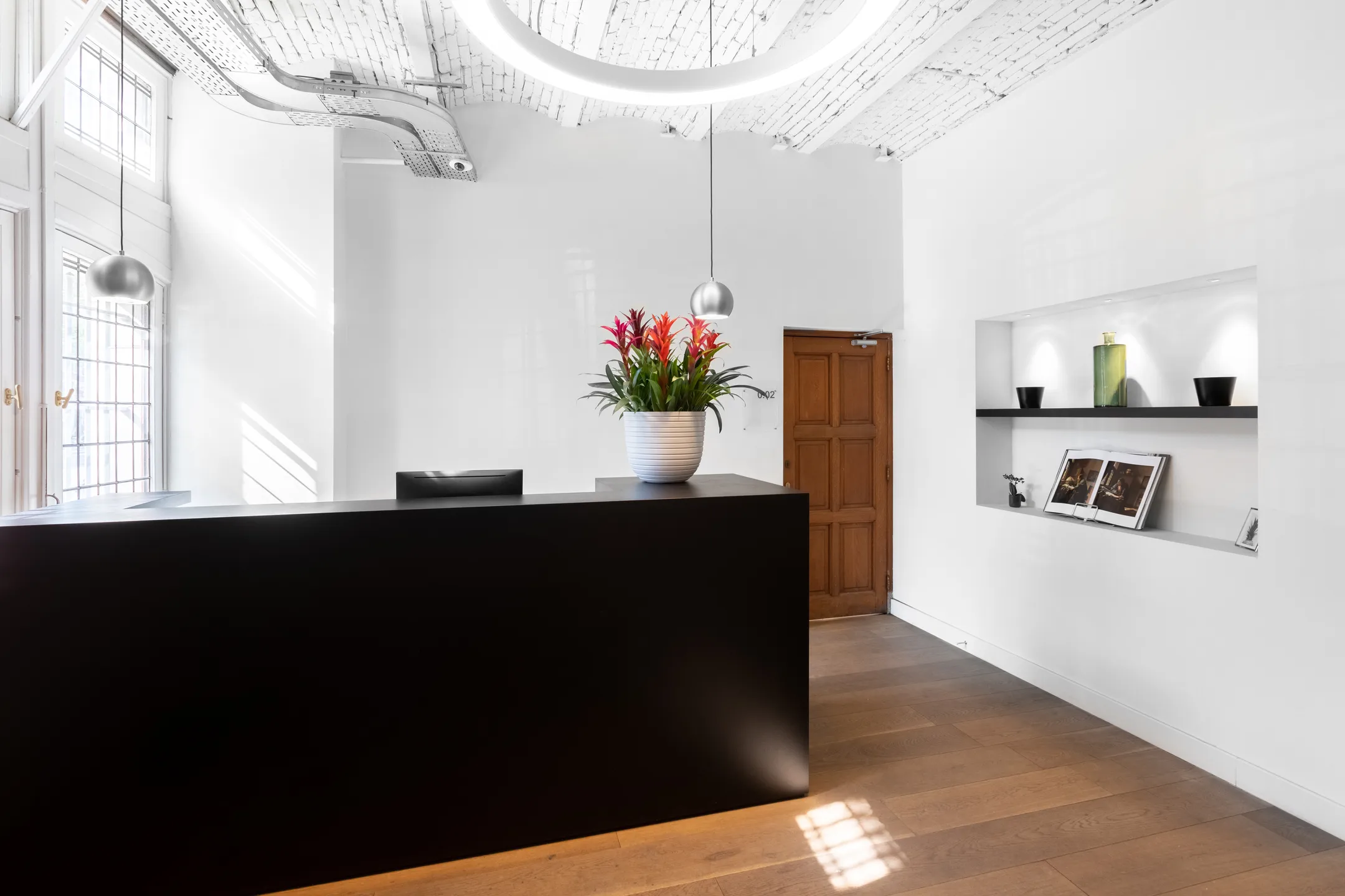 Een moderne receptie met een zwarte balie, een pot met kleurrijke bloemen en een plank met decoratieve elementen aan de muur.