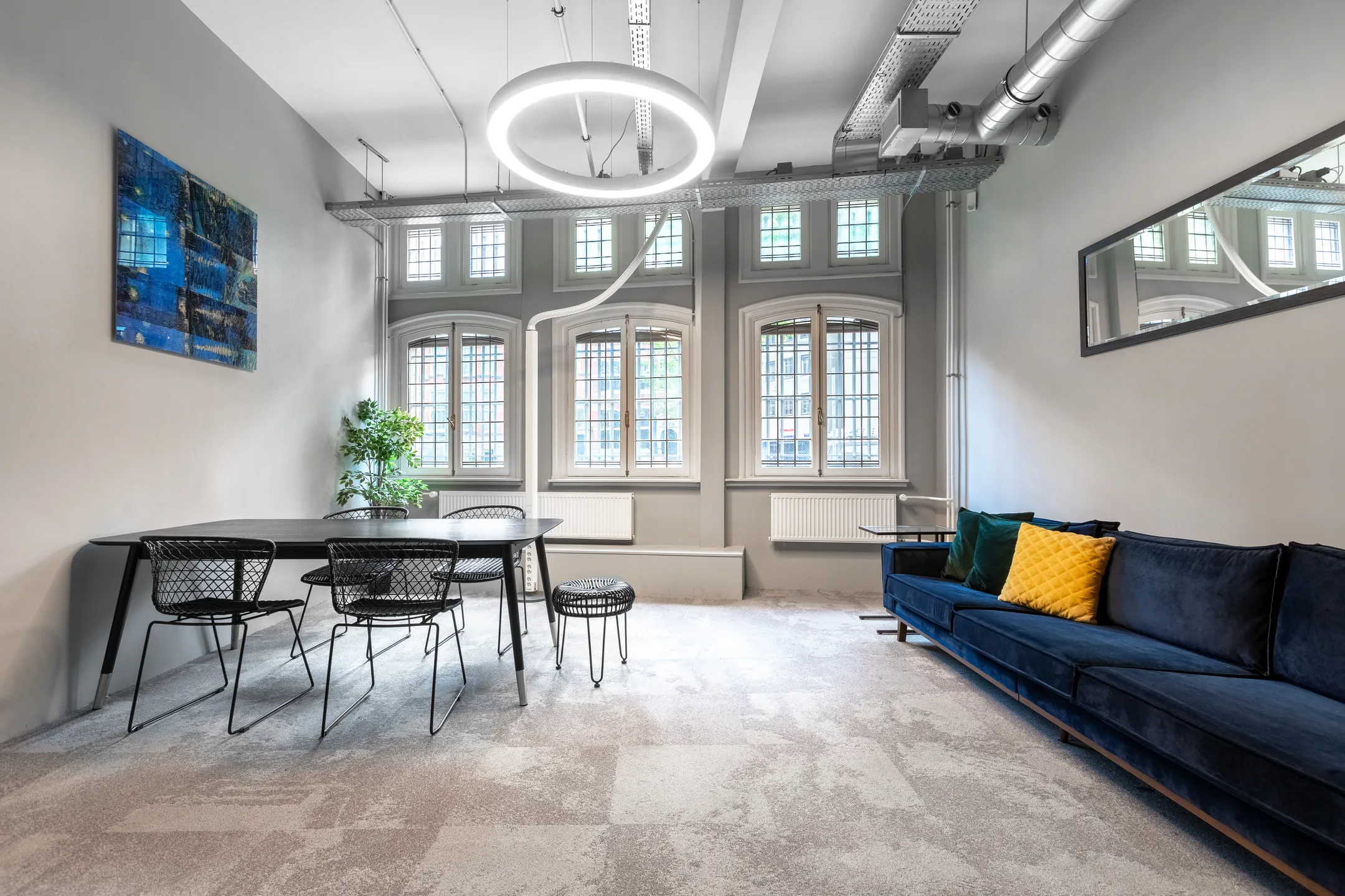 Een modern ingerichte kamer met een tafel, stoelen, een blauwe bank en grote ramen.