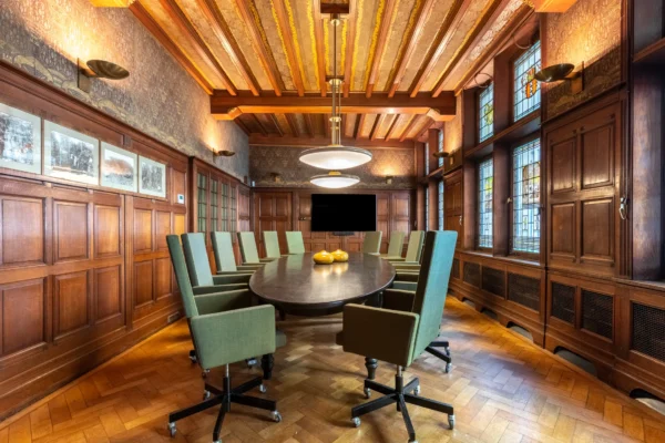 Een elegante vergaderruimte met een ovale houten tafel, omgeven door groene stoelen en decoratieve houten panelen.