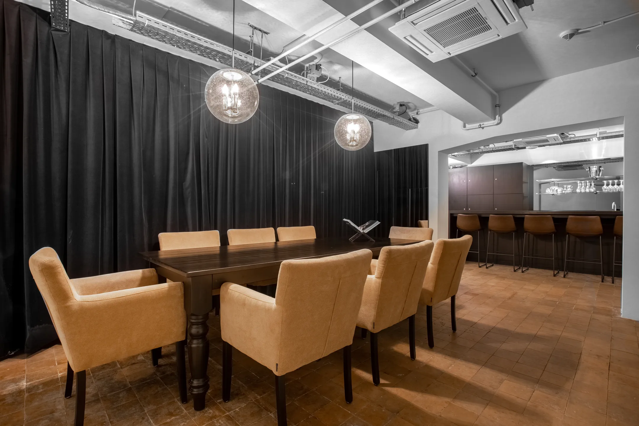 Een moderne eetkamer met een houten tafel, beige stoelen en een bar met krukken op de achtergrond.