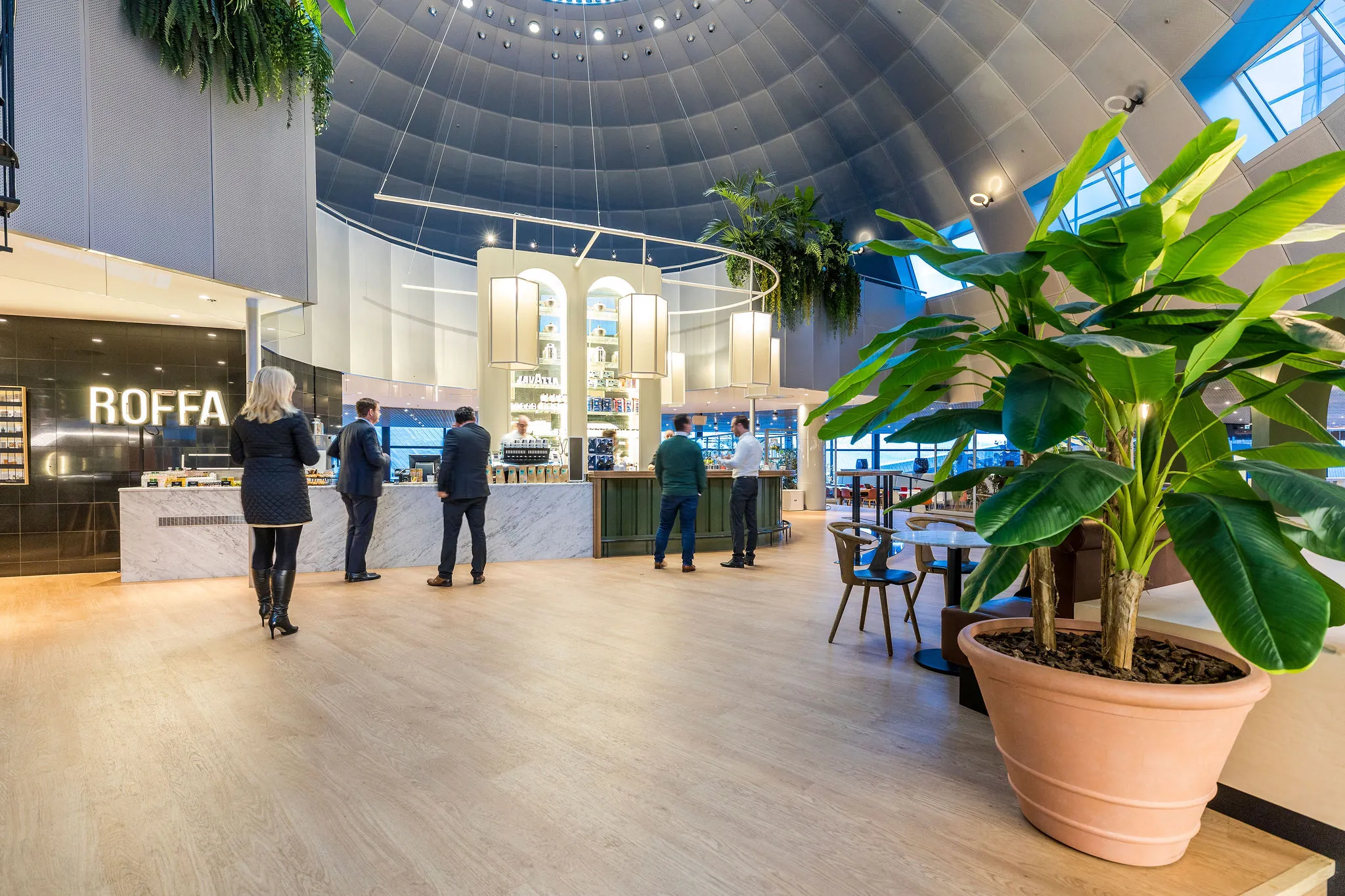 Modern ingericht café genaamd ROFFA met mensen aan de balie in een open, koepelvormige ruimte met veel groen.