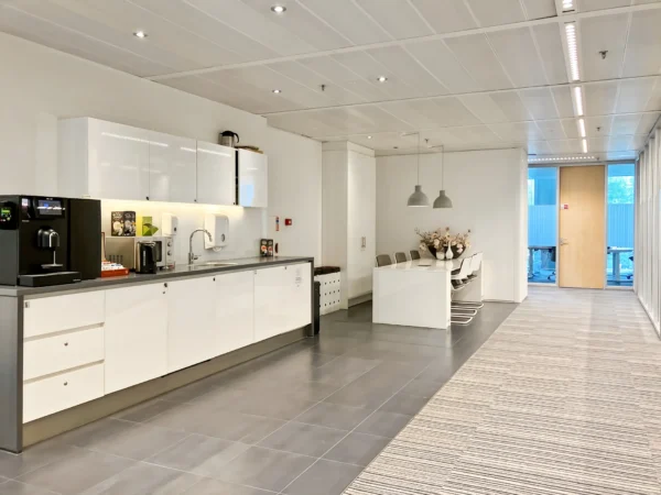 Een moderne kantoor keuken met een koffiezetapparaat, kasten en een eettafel met stoelen.