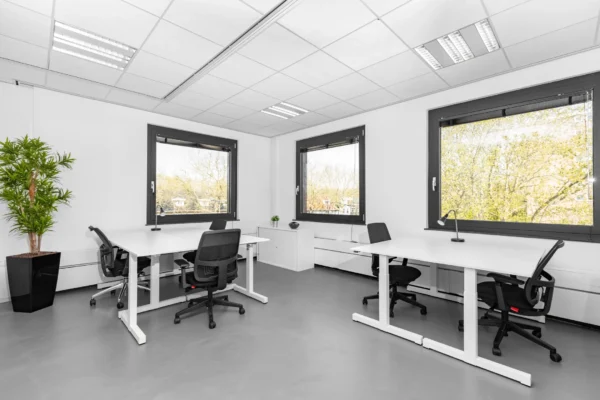 Een lichte en moderne kantoorruimte met bureaus, stoelen en grote ramen.