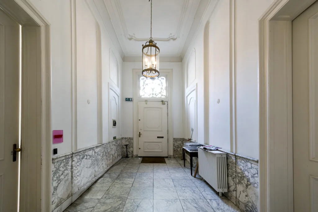 Lichte marmeren hal in een grachtenpand aan de Herengracht met hoge plafonds, klassieke deuren en een hangende lantaarnlamp.