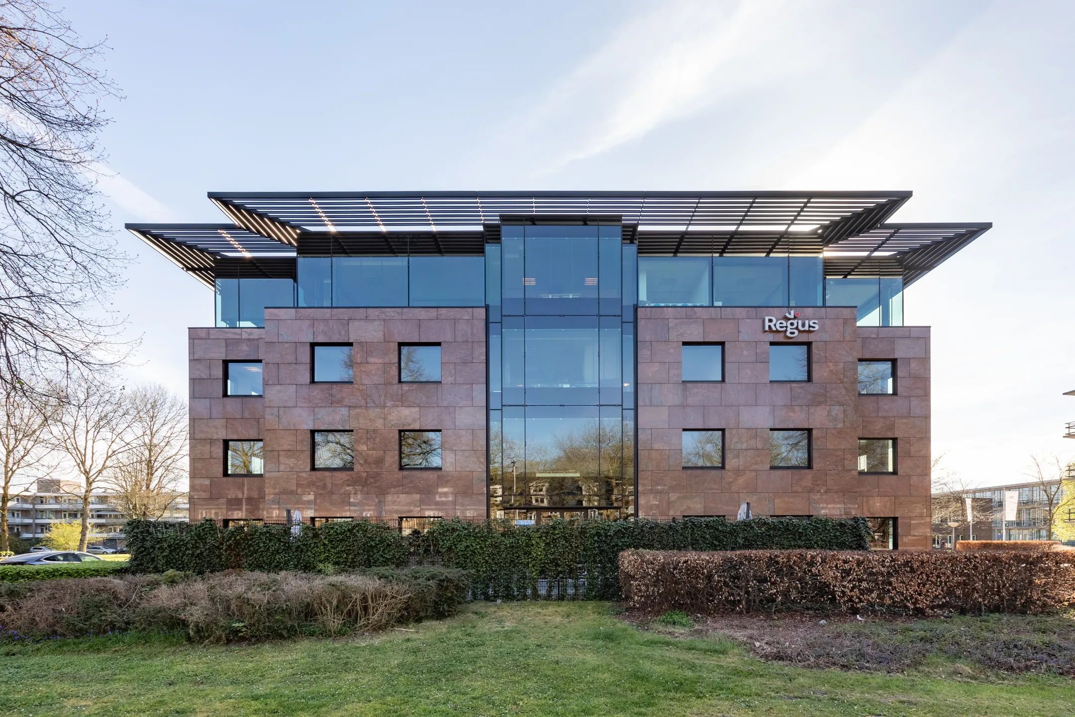 Een modern kantoorgebouw van Regus met grote glazen ramen en een stenen gevel op een zonnige dag.