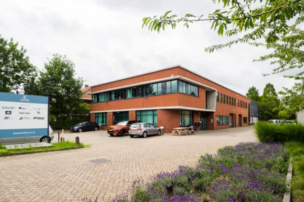 Een modern kantoorgebouw met parkeerplaats en een bord met bedrijfslogo's aan de Kanaalweg.