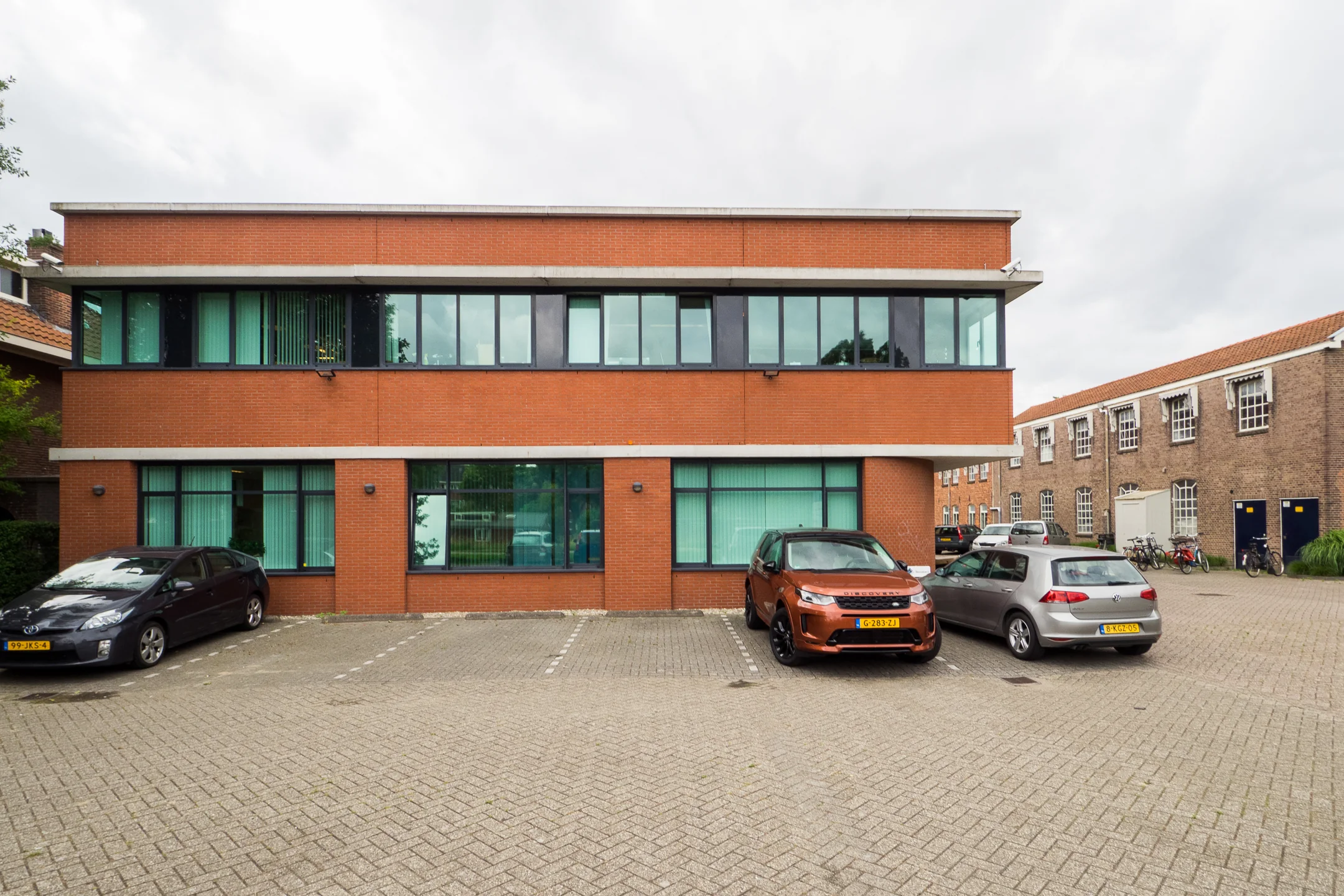 Een bakstenen kantoorgebouw met geparkeerde auto's op de Kanaalweg.