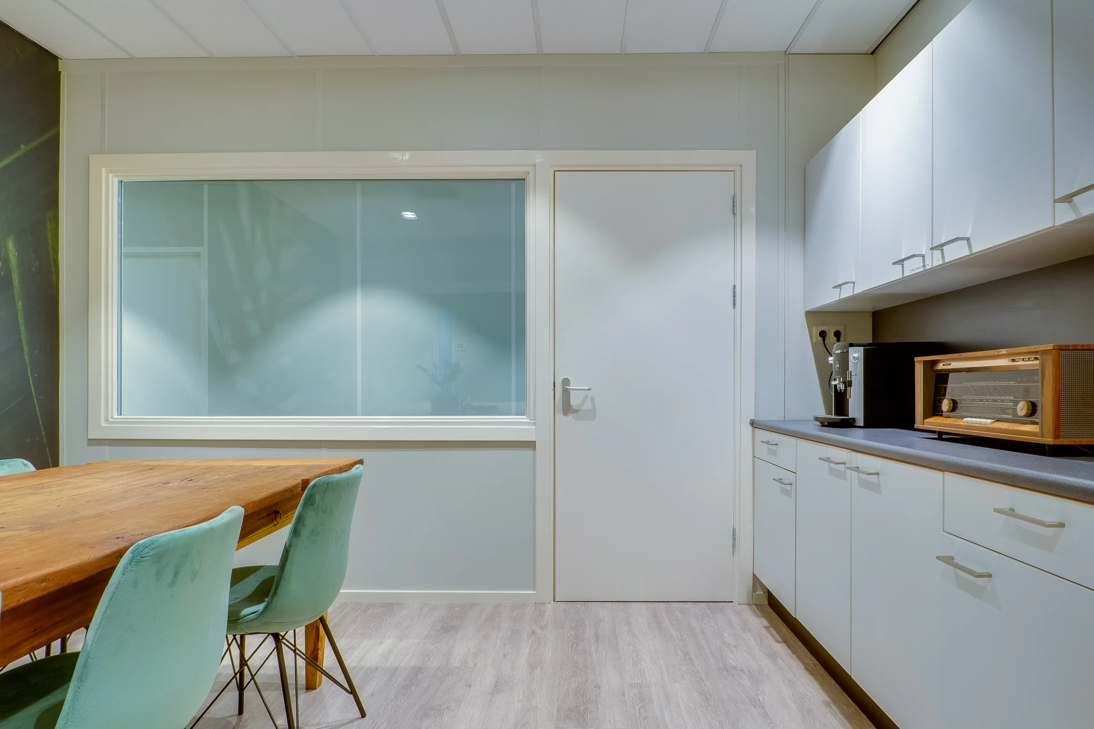 Een moderne keuken met wit aanrecht, een houten tafel en mintgroene stoelen.