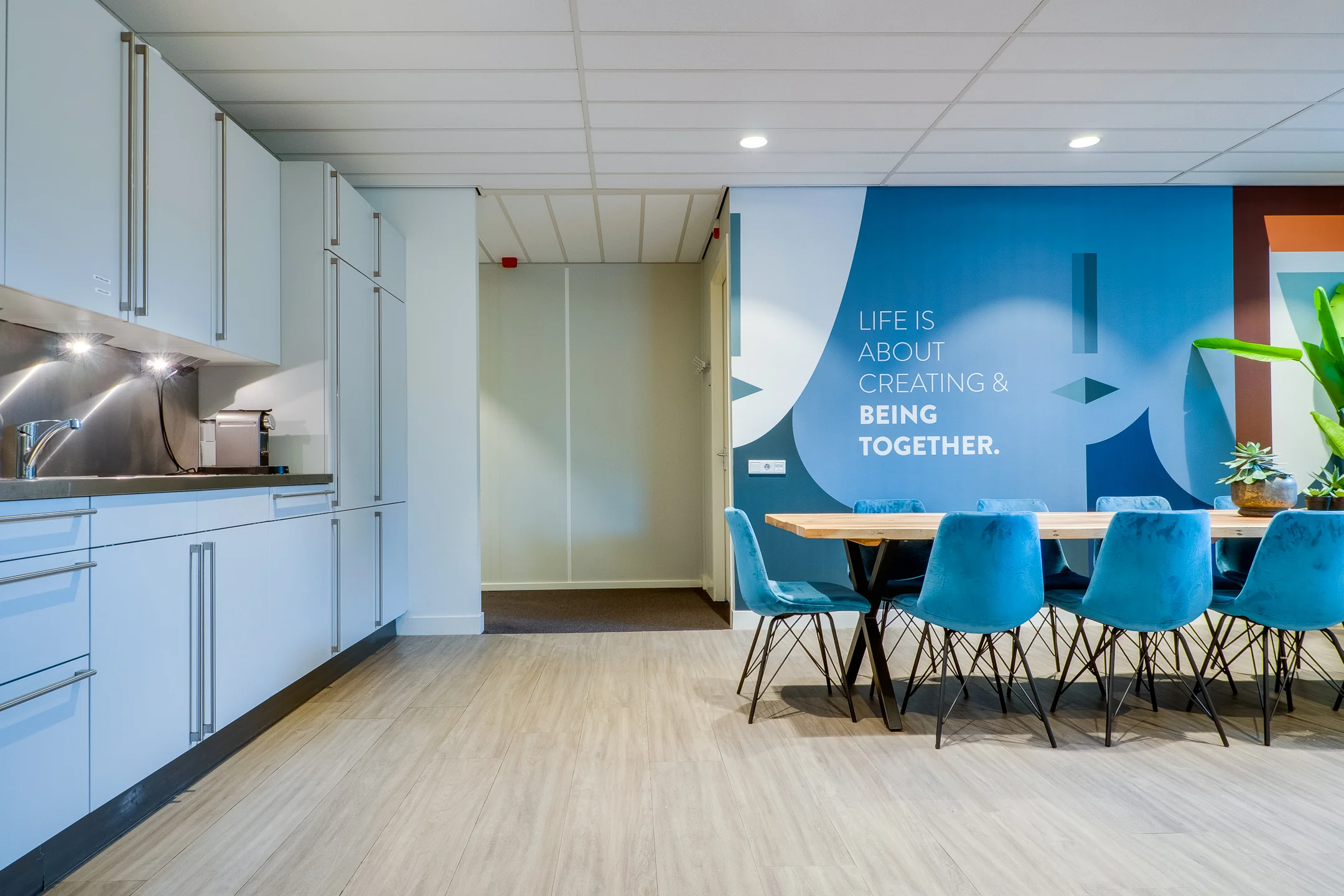 Een moderne kantoorruimte met keuken, blauwe stoelen en een inspirerende boodschap op de muur.