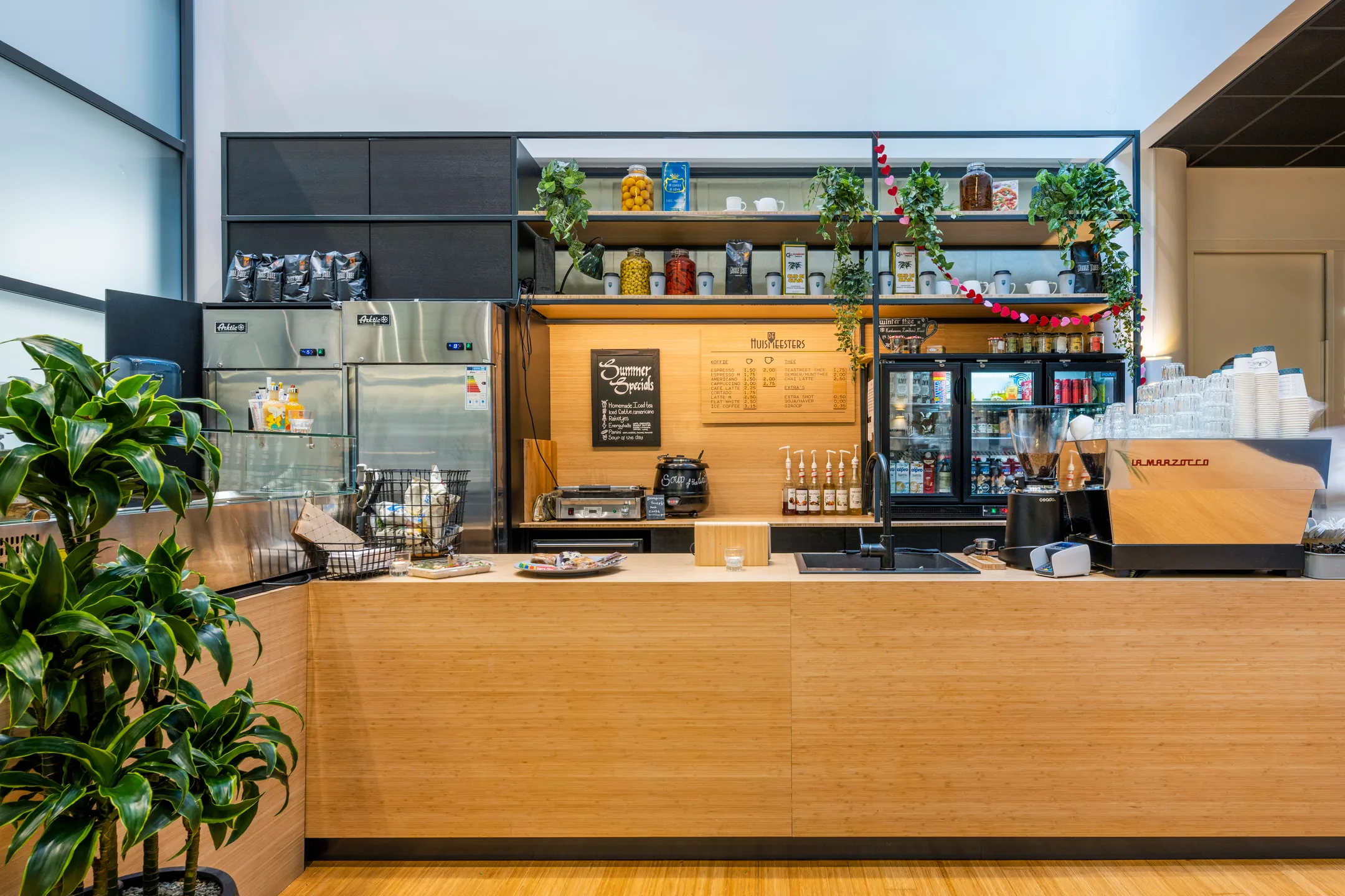 Een moderne koffiebar met houten toonbank, planten en een espressomachine.